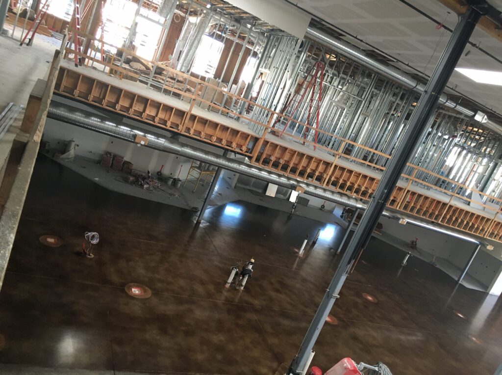 A large room with a high-shine marbled brown concrete floor, showing reflections of ceiling lights and colored walls, with a fire extinguisher mounted on a column, giving the space a functional yet polished appearance.