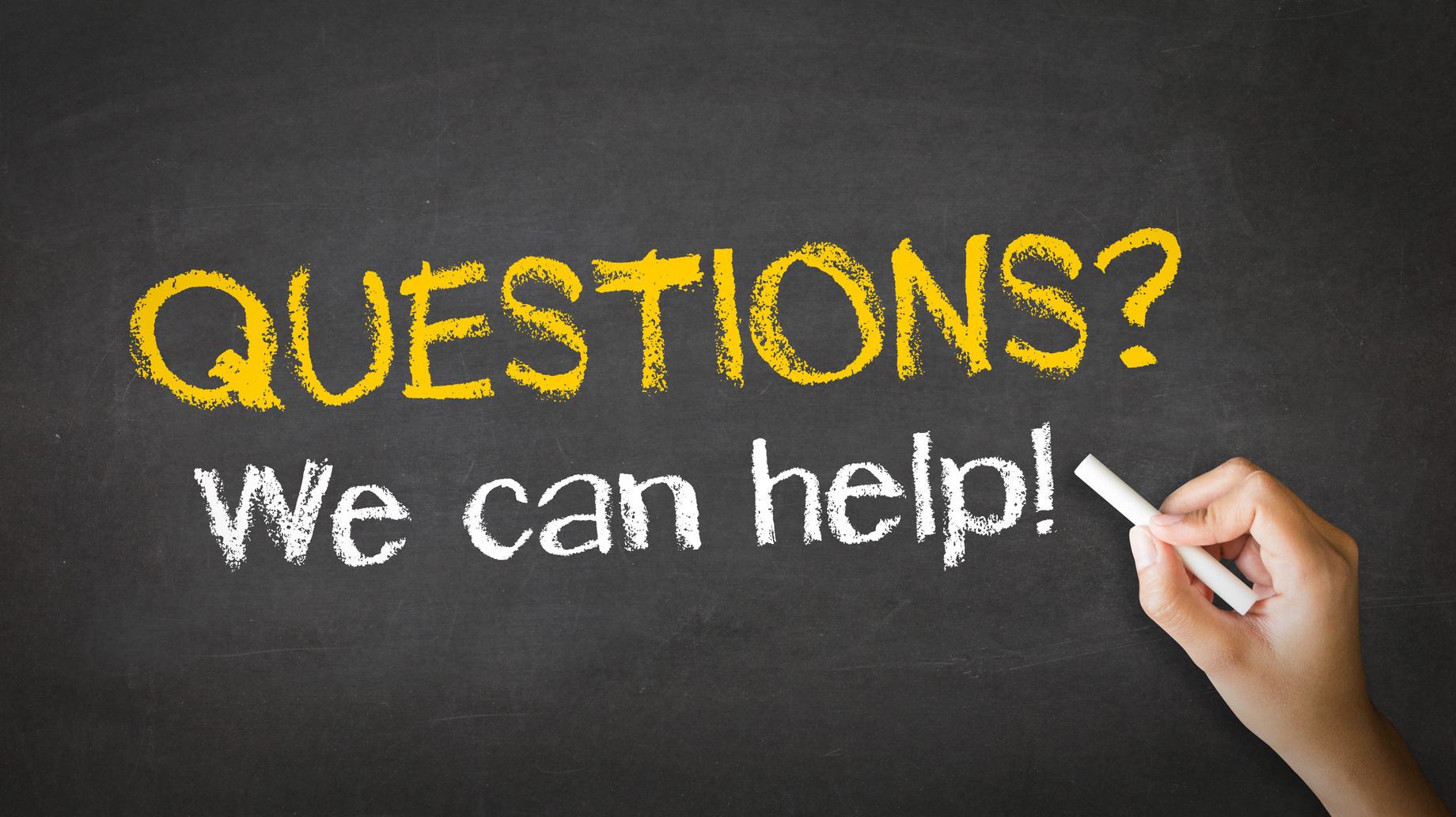 A person's hand holding white chalk against a blackboard with the words 'QUESTIONS? We can help!' written in bold, yellow chalk. The text on the blackboard is clear and stands out, suggesting an offer of assistance to decide between polyaspartic and epoxy topcoats for concrete floors.