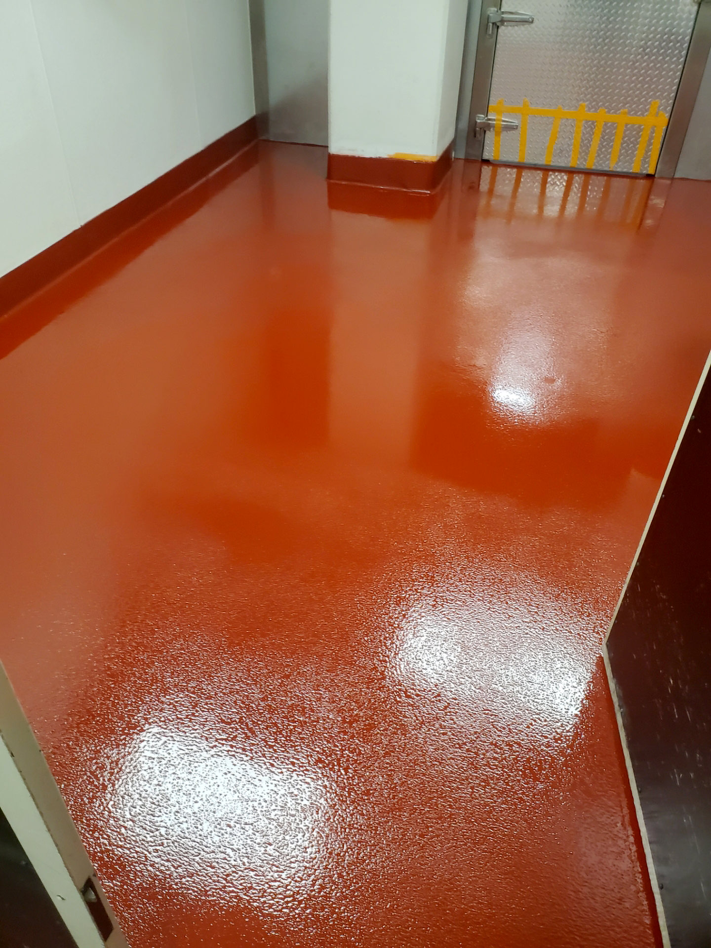 A room with glossy red epoxy flooring reflecting overhead lighting, featuring clean white walls with multiple water outlets, possibly in a commercial or industrial setting.