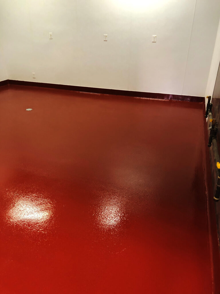A room with glossy red epoxy flooring reflecting overhead lighting, featuring clean white walls with multiple water outlets, possibly in a commercial or industrial setting.