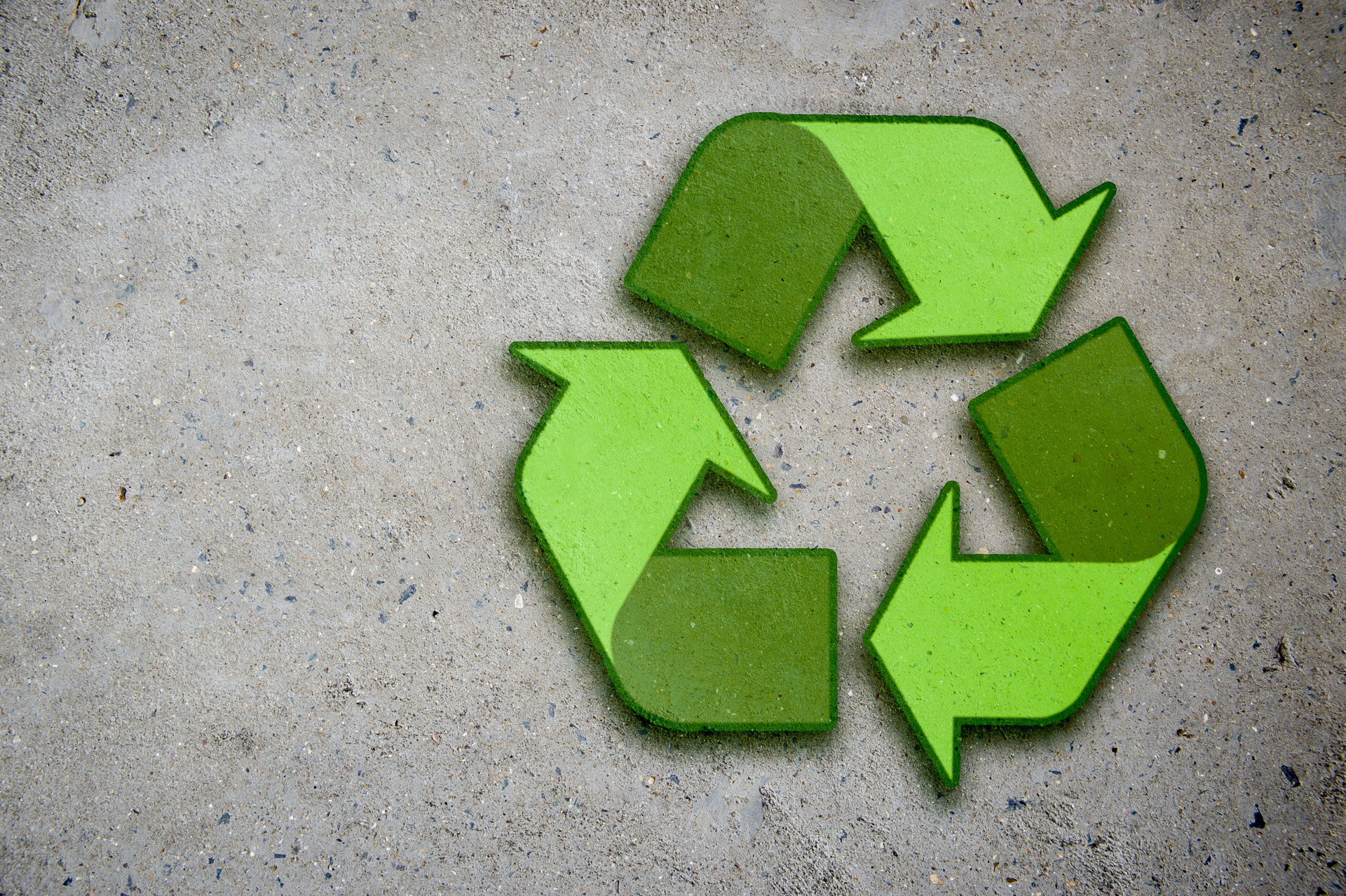 A vibrant green recycling symbol composed of three chasing arrows on a rough concrete surface, representing the concept of sustainability and environmental conservation of concrete and recycled aggregates. Preserve your concrete with an epoxy coating.