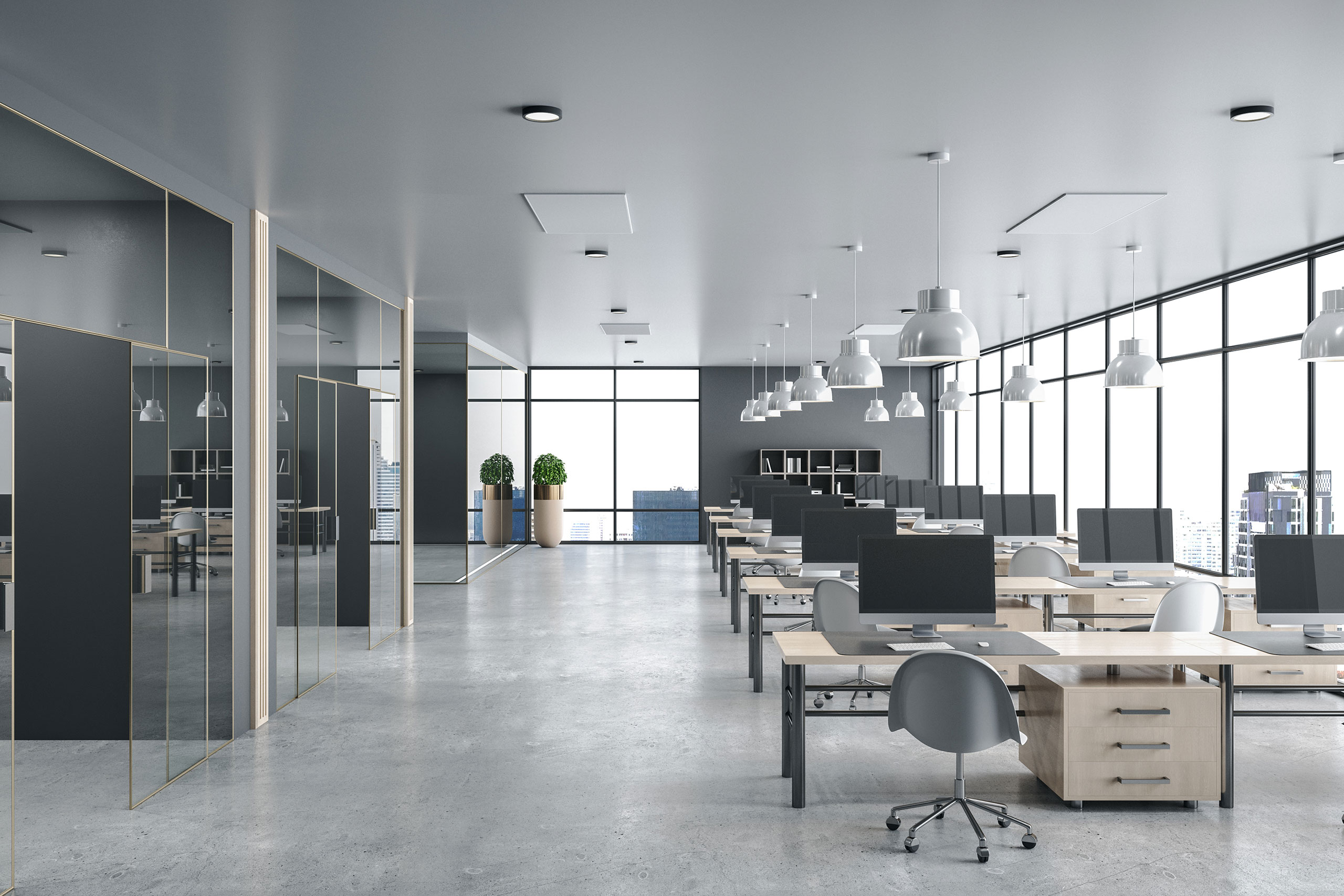 Modern open-plan office with rows of wooden desks equipped with desktop computers and gray ergonomic chairs on a polished concrete floor. Large floor-to-ceiling windows line the right wall, offering views of city skyscrapers. The ceiling features multiple white pendant lights, and two potted plants stand near the windows at the back. Glass-walled private offices or meeting rooms are on the left side. The space has a sleek, minimalistic design with neutral gray and natural wood tones.