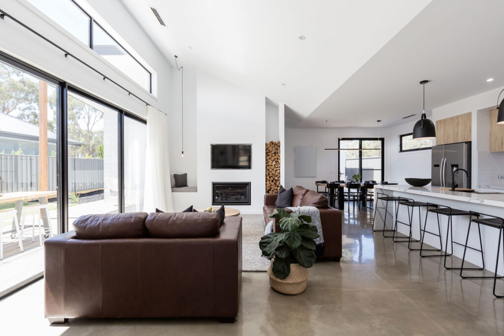 Bright open-plan living area with polished concrete floors, brown leather sofas, and modern kitchen with island seating.
