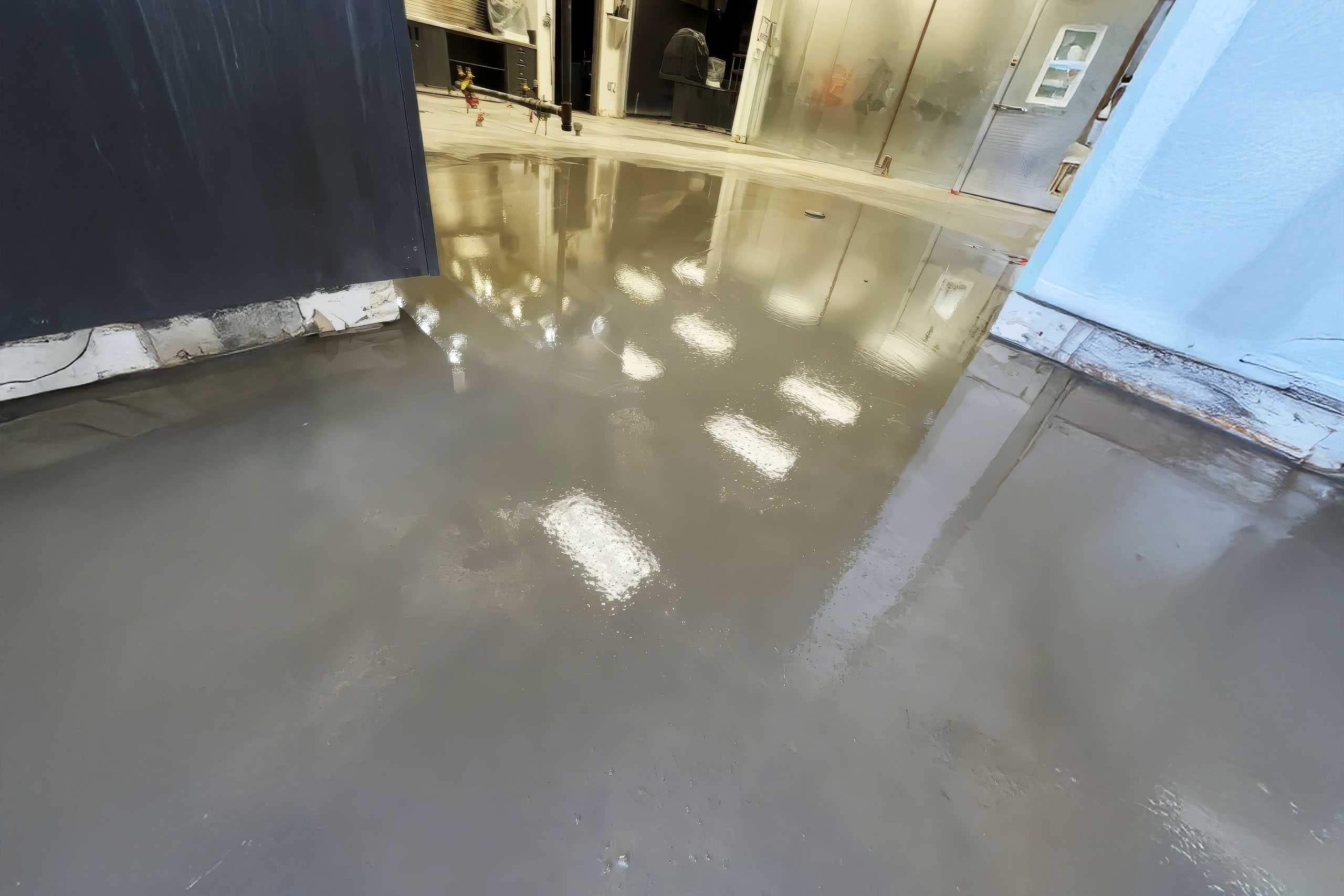 Overlay_wide.jpg Freshly poured and leveled concrete overlay reflecting ceiling lights inside a commercial building under renovation.