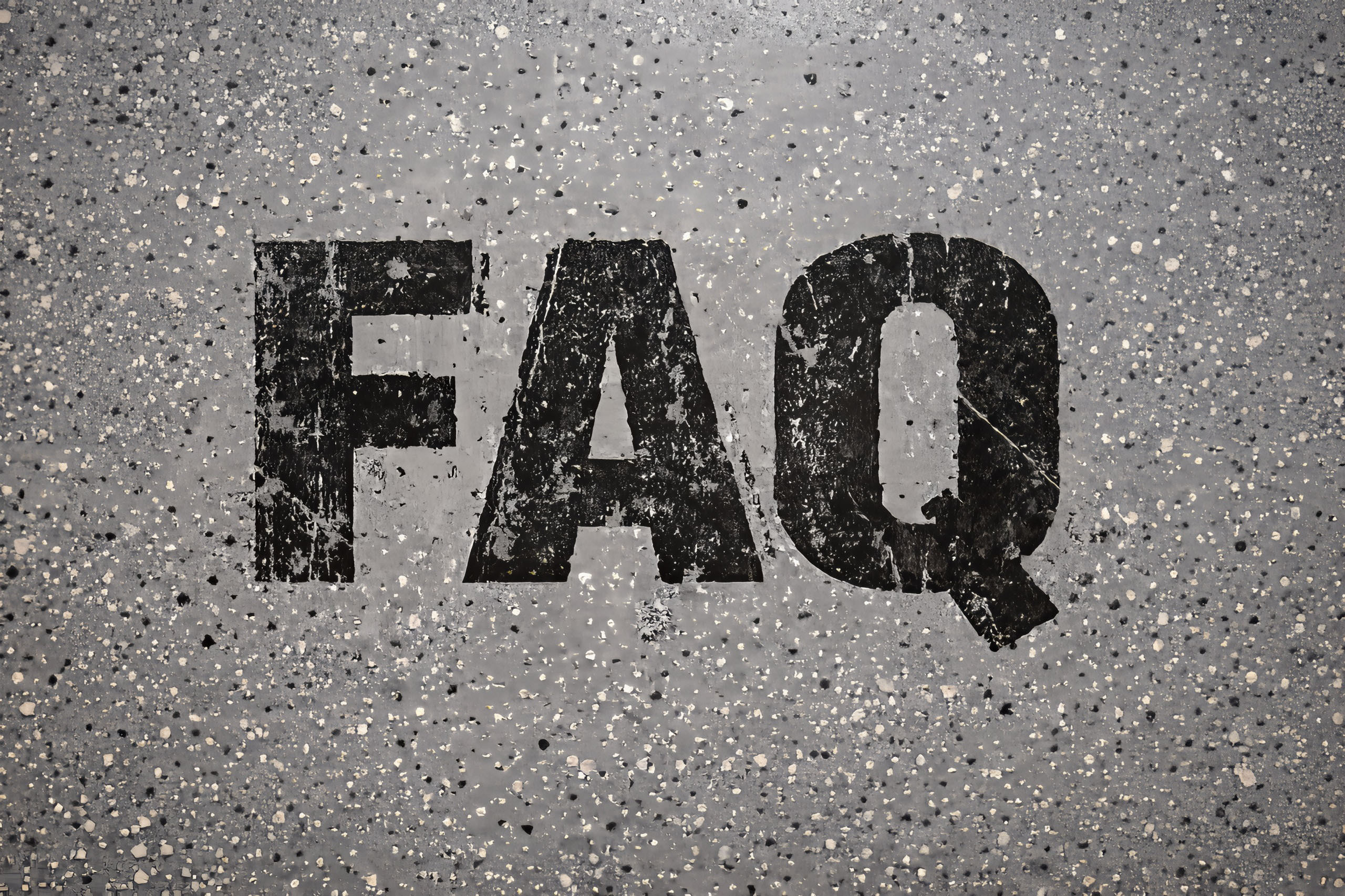 Overhead view of a gray epoxy garage floor with black, distressed ‘FAQ’ lettering embedded directly into the coating, showing a gritty, industrial texture.