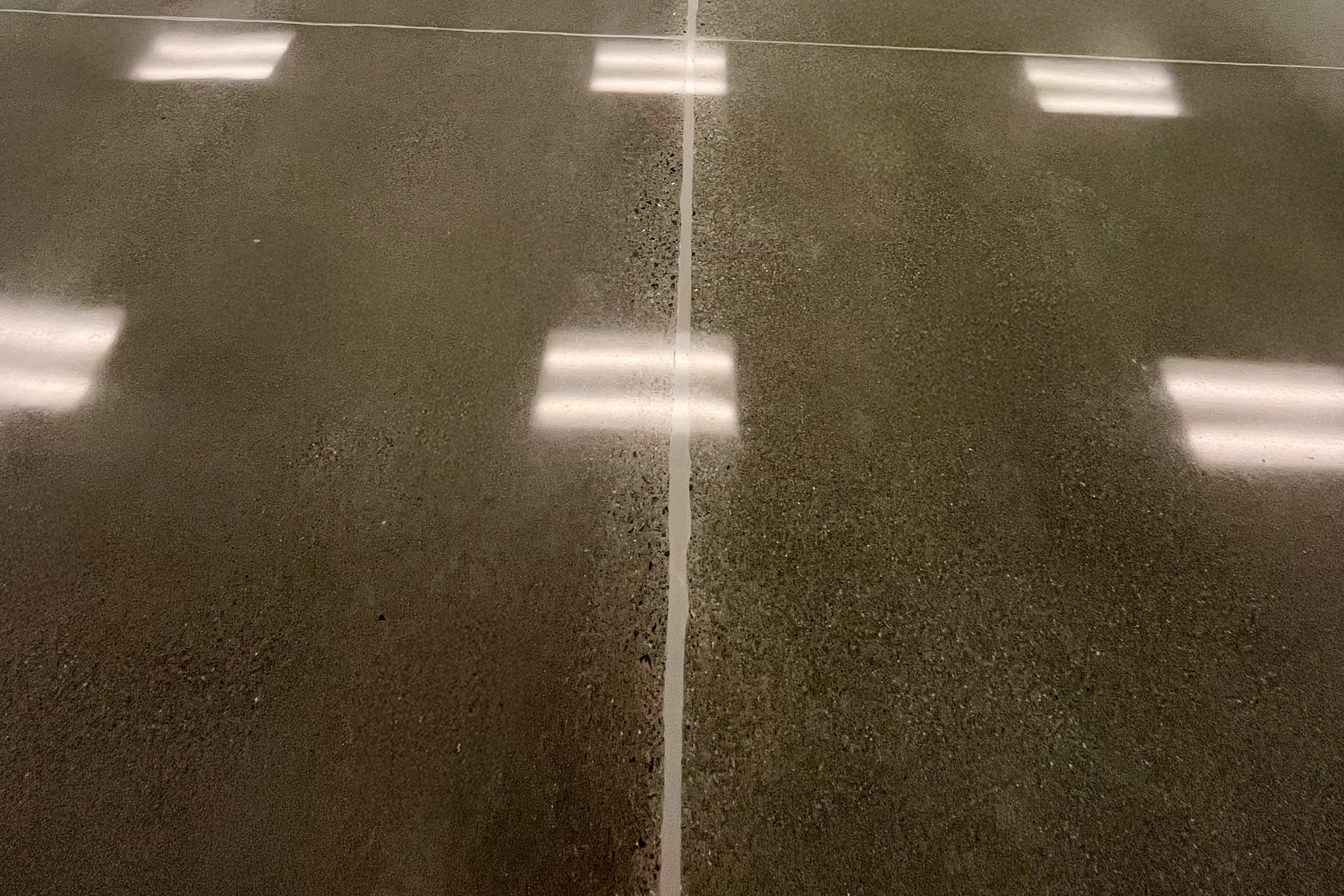 Polished concrete floor with a visible joint line and reflections of overhead lights.